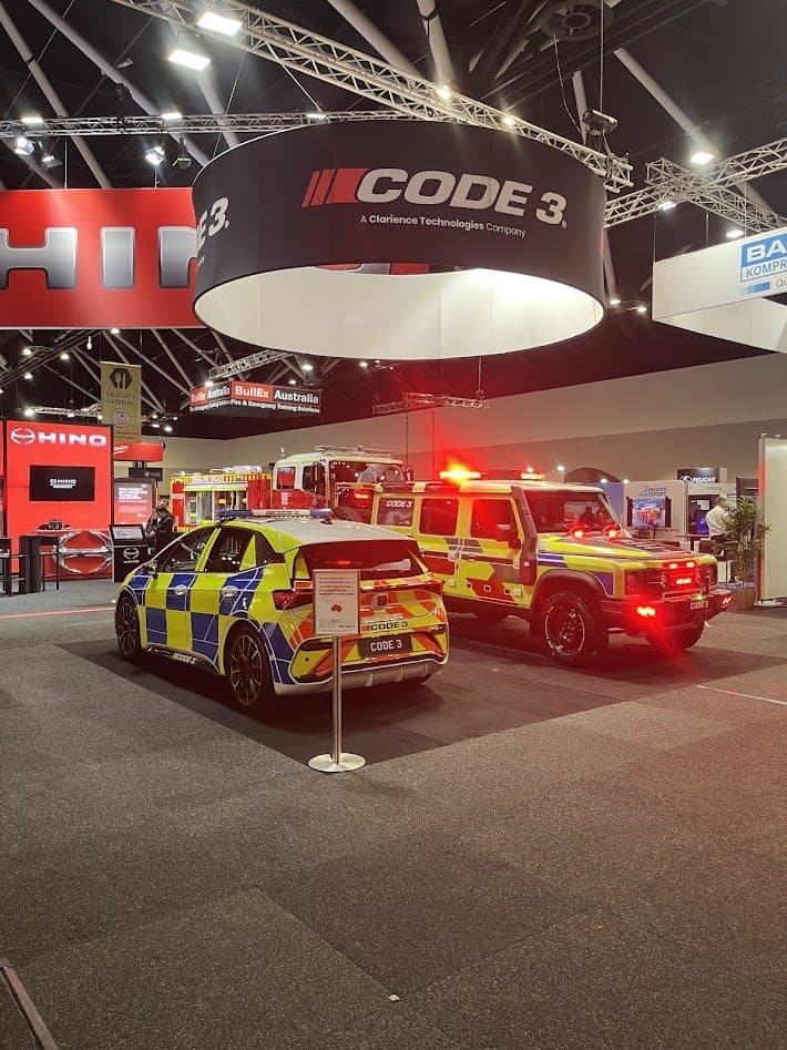 Code 3 exhibition stand with liveried emergency vehicles under a circular overhead banner