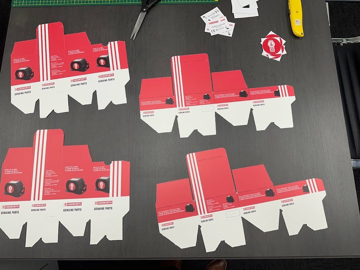 Four unfolded packaging die lines for back-up alarms in Kenworth Genuine Parts livery